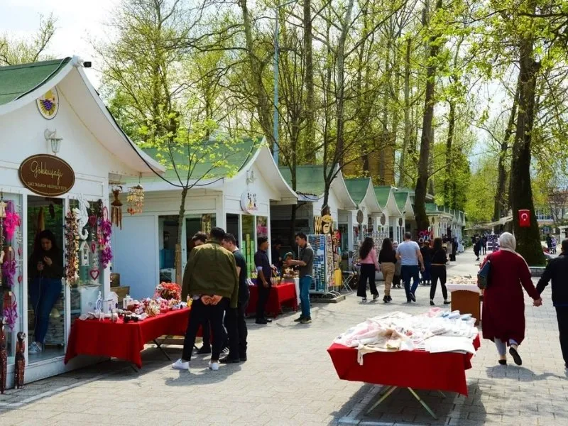 Ağaçlar altında sıralanan ahşap dükkânlar ve tezgâhlar